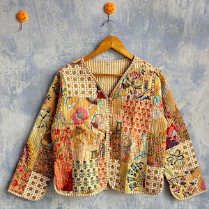 Può includere: Una giacca trapuntata a maniche lunghe con un design patchwork caratterizzato da vari motivi floreali e geometrici nei toni del giallo, rosso e blu. La giacca presenta uno scollo a V, una chiusura frontale con bottoni e una fodera a righe.