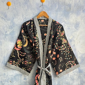Könnte beinhalten: Ein schwarzer Kimono-Bademantel mit einem Blumenmuster in Rosa-, Gelb- und Grüntönen. Das Kleidungsstück verfügt über einen weiß-schwarz gestreiften Besatz entlang der Vorderseite, an den Ärmelbündchen und am passenden Bindegürtel.