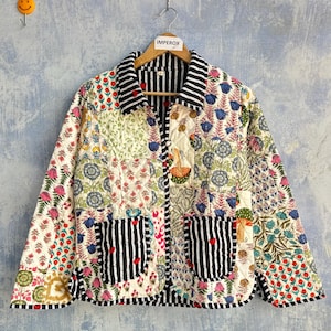 Könnte beinhalten: Eine gesteppte Jacke mit einem Patchwork aus Blumen- und Pflanzenmustern in Rot-, Blau-, Grün- und Gelbtönen. Das Kleidungsstück hat einen schwarz-weiß gestreiften Kragen, Ärmelbündchen, Saum und zwei Vordertaschen, verziert mit kleinen roten Herzen.
