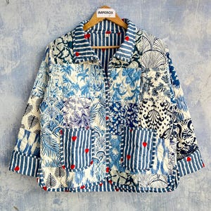 May include: A quilted jacket featuring a patchwork design of blue and white patterns, including stripes, tropical leaves, and floral motifs. The garment has a collar, long sleeves with striped cuffs, and two front pockets, all accented with small red hearts.