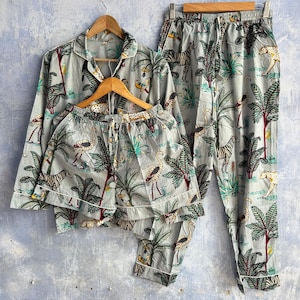 Könnte beinhalten: Ein hellgrauer Schlafanzug bestehend aus einem langärmeligen Hemd mit Knopfleiste, passenden Shorts und einer langen Hose. Der Stoff zeigt ein Dschungel-Muster mit Zebras, Leoparden und Flamingos zwischen Palmen, abgesetzt mit einer weißen Paspelierung.