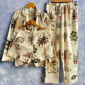 May include: A set of cream-colored pajamas featuring a repeating botanical print of trees and plants in shades of green, brown, and red. The set includes a long-sleeve button-down shirt, a pair of matching shorts, and a pair of long trousers.