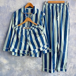 May include: A pajama set consisting of a long-sleeve button-down shirt, a pair of shorts, and a pair of long pants. Each piece features a vertical striped pattern in alternating shades of dark blue and light blue, with white piping details.
