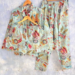 May include: A light blue pyjama set featuring a long-sleeve button-down shirt, matching long trousers, and shorts. The fabric is decorated with a vibrant, multi-coloured floral and paisley pattern in shades of red, yellow, and dark blue.
