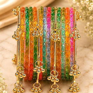 Op de afbeelding: Een set veelkleurige, doorschijnende armbanden met een getextureerd, gefacetteerd oppervlak. De collectie bevat levendige tinten oranje, groen, geel, roze en blauw, geaccentueerd met goudkleurige metalen staven en bungelende belletjes.