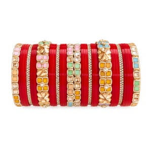 Puede incluir: Un conjunto de brazaletes apilados que presenta numerosas pulseras rojas lisas intercaladas con bandas decorativas. Estas bandas incluyen motivos florales de metal dorado con incrustaciones cuadradas en tonos pastel y cristales.