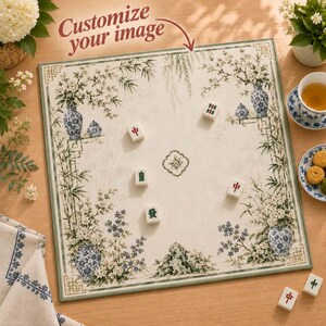 May include: A square mahjong mat featuring a cream-coloured surface with a botanical border of blue and white porcelain vases, flowers, and bamboo. The text "Customize your image" is printed at the top. Five mahjong tiles are scattered on the mat.