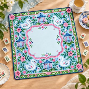 May include: A square game mat featuring a light blue centre bordered by a pink scalloped frame. The border displays a repeating pattern of white swans, blue pagodas, and pink flowers with green leaves on a light blue background with a dark blue edge.