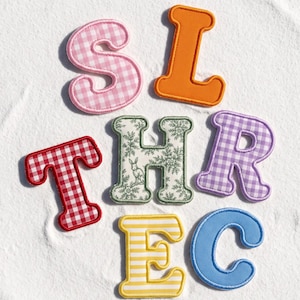May include: A collection of seven embroidered fabric letter patches featuring various patterns and colors. The letters include a pink gingham S, a solid orange L, a red gingham T, a green floral H with a rabbit, a purple gingham R, a yellow striped E, and a solid blue C.