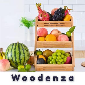 May include: A three-tiered bamboo fruit stand filled with assorted fresh produce including a dragon fruit, grapes, peaches, oranges, and green grapes. The word "Woodenza" is printed in dark blue letters at the bottom of the image.