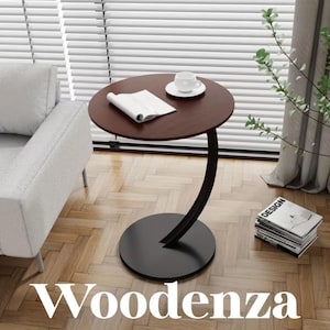 May include: A round, dark brown wooden side table with a C-shaped black metal base. The tabletop holds an open white book and a white ceramic coffee cup on a saucer. The table stands on a light-colored wooden floor next to a gray sofa.
