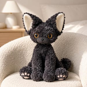 Può includere: Un peluche a forma di gatto realizzato in filato testurizzato grigio antracite scuro con grandi orecchie a punta dotate di interno color crema. Il gatto ha occhi color ambra, un piccolo naso nero e cuscinetti visibili sulle zampe anteriori.