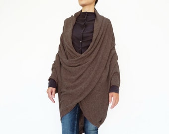 May include: A brown knit wrap with a cowl neck and long sleeves. The wrap is worn over a black button-down shirt and blue jeans. The model is wearing brown heeled boots and sunglasses.