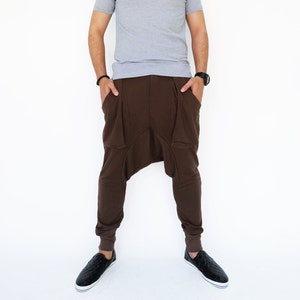 May include: A man wearing a gray polo shirt and brown pants with a unique design. He is standing with his hands in his pockets and looking to the right.