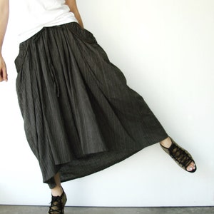 May include: A woman wearing a white tank top and a long, dark gray skirt with vertical stripes. She is wearing brown sandals.