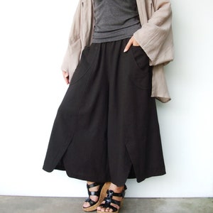 May include: A woman wearing a black wide-leg pants with a long, loose-fitting, light brown cardigan. She is wearing black sandals with cork wedges.
