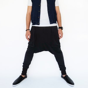 Puede incluir: Un hombre con una camiseta blanca, un chaleco vaquero azul oscuro y pantalones negros con un diseño único. Lleva zapatos negros.