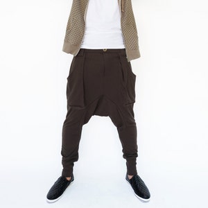 Könnte beinhalten: Ein Mann trägt ein braunes Kapuzenpullover mit einem weißen T-Shirt darunter. Er trägt eine braune Hose mit großen Taschen und schwarze Schuhe.