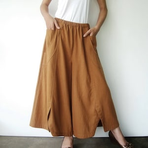 May include: A pair of wide-legged, brown linen pants with a relaxed fit and large pockets. The pants have a drawstring waist and a slightly flared hem.