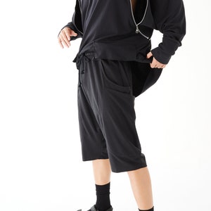 Puede incluir: Una sudadera con capucha negra con mangas con cremallera y un par de pantalones cortos negros a juego. El modelo lleva calcetines y sandalias negras.