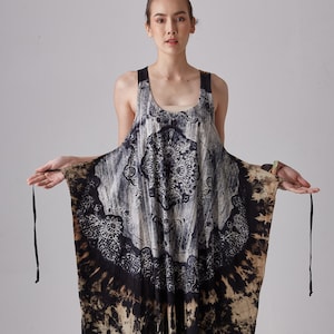 May include: A long, flowing black and beige dress with a tie-dye pattern and a large circular design in the center. The dress has thin straps and a scoop neck.