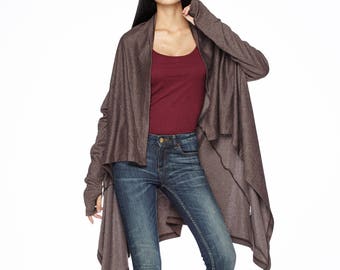 May include: A brown knit cardigan with long sleeves and a draped front. The cardigan is worn over a maroon tank top and blue jeans. The model is wearing black heeled ankle boots.