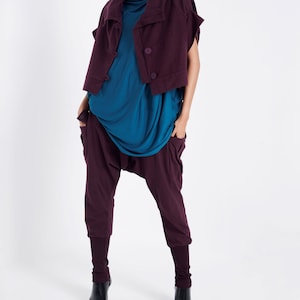 Puede incluir: Una mujer con una blusa azul turquesa, pantalones burdeos y una chaqueta corta burdeos con un cuello grande. Lleva botas de tacón negras.