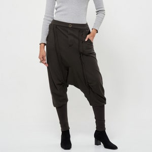 May include: A woman is wearing a gray turtleneck sweater and brown, loose-fitting pants with a unique design. The pants have a wide leg and a gathered detail at the ankles.