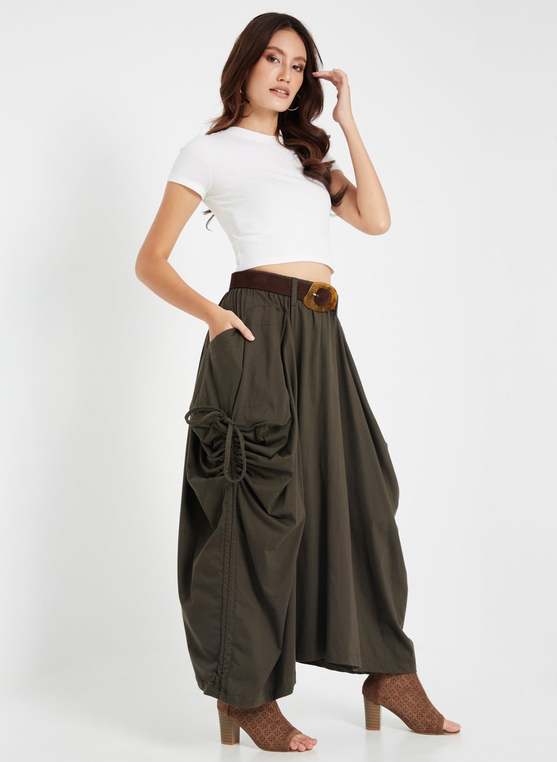 Puede incluir: Una mujer con un top blanco corto y una falda verde oscuro con pliegues y un cintur&oacute;n marr&oacute;n. Lleva zapatos de tac&oacute;n marrones.