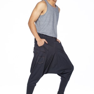 May include: A man wearing a gray tank top and dark blue pants with a unique design. He is wearing black sneakers.