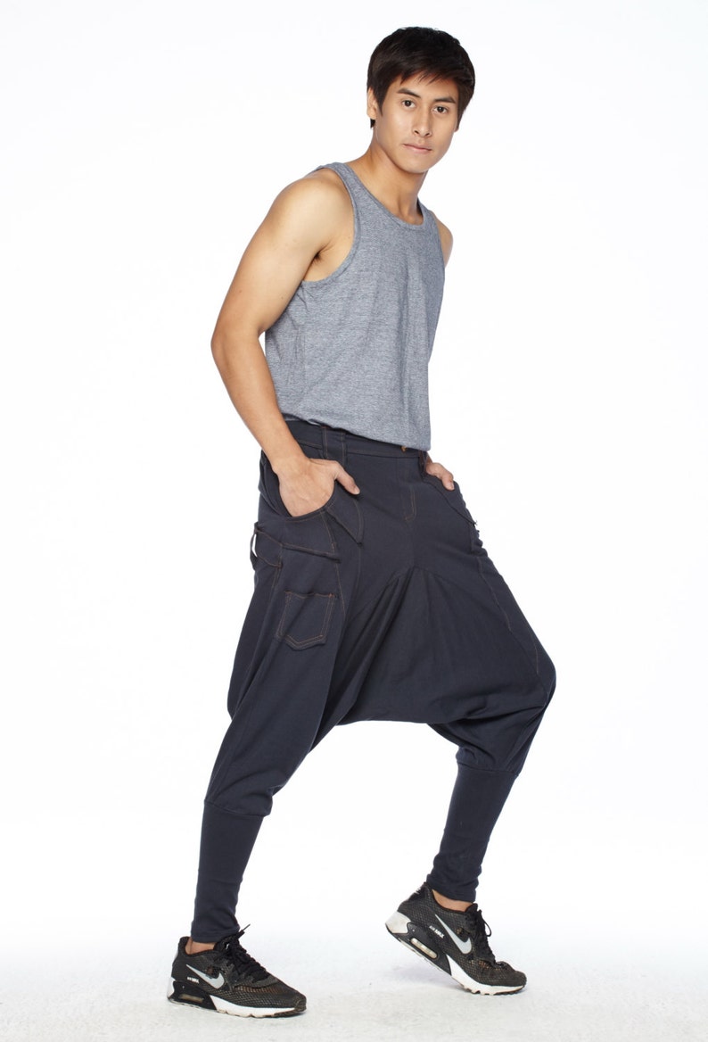 May include: A man wearing a gray tank top and dark blue pants with a unique design. He is wearing black sneakers.