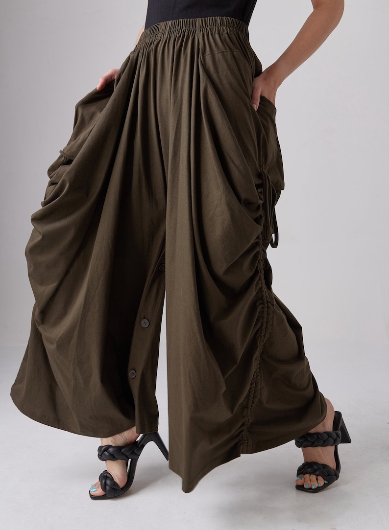 May include: A pair of olive green wide-leg pants with a drawstring waist and a button-up front. The pants are gathered and have a loose, flowing fit.