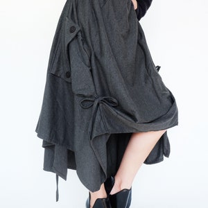 May include: A gray asymmetrical skirt with a gathered design and a button detail. The skirt is made of a soft, drapey fabric and has a relaxed fit.