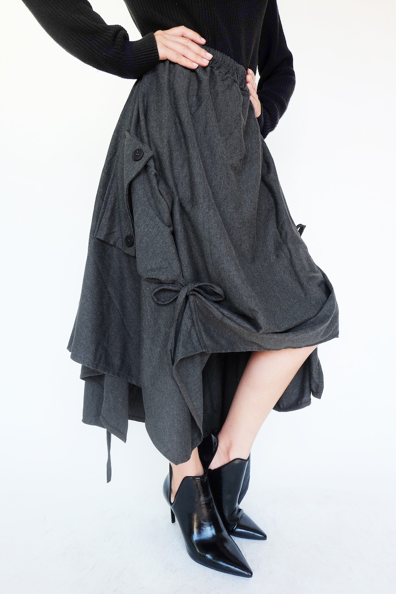 May include: A gray asymmetrical skirt with a gathered design and a button detail. The skirt is made of a soft, drapey fabric and has a relaxed fit.