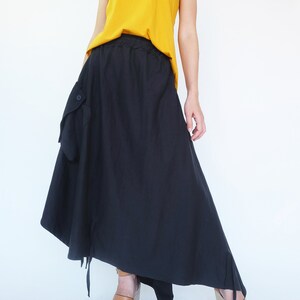 May include: A black asymmetrical skirt with a large pocket on the left side. The skirt has a drawstring waistband and is paired with a mustard yellow tank top.