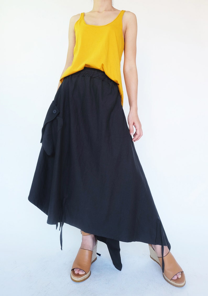 May include: A black asymmetrical skirt with a large pocket on the left side. The skirt has a drawstring waistband and is paired with a mustard yellow tank top.