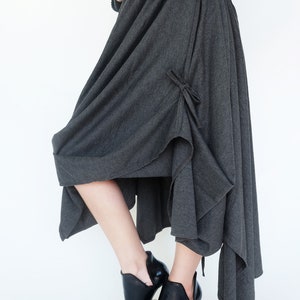 May include: A charcoal gray asymmetrical skirt with a tie detail at the side. The skirt is made of a soft, drapey fabric and has a relaxed fit.