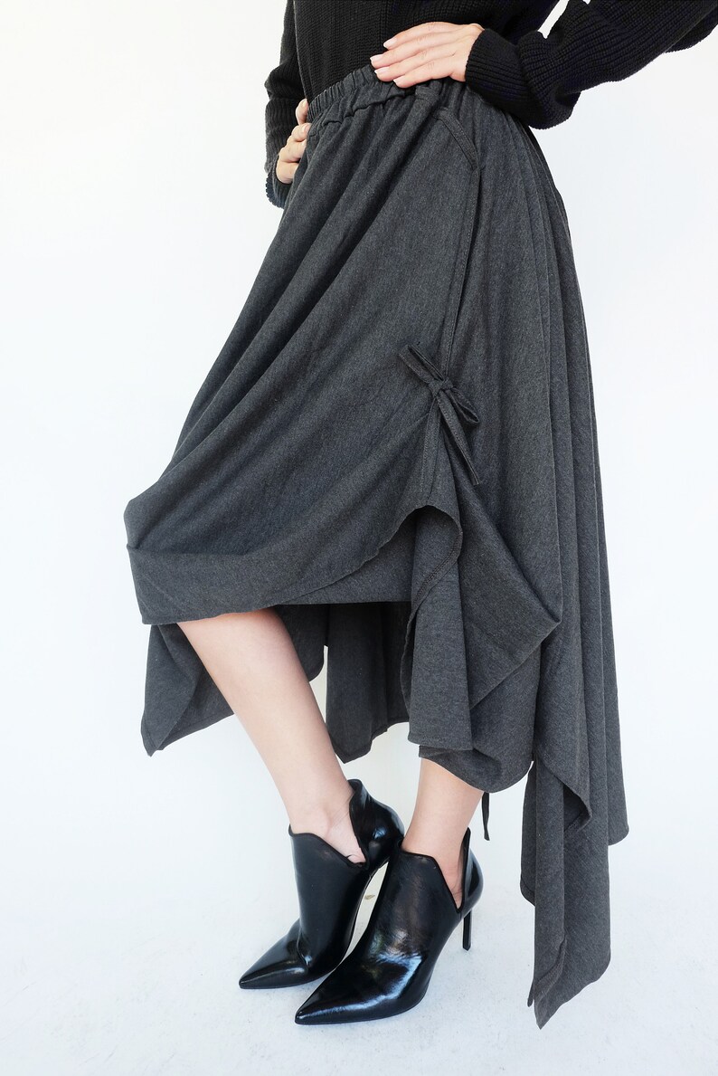 May include: A charcoal gray asymmetrical skirt with a tie detail at the side. The skirt is made of a soft, drapey fabric and has a relaxed fit.