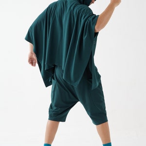 May include: A person wearing a dark green hooded poncho with matching shorts. The poncho has a long, flowing design and the shorts are loose-fitting.