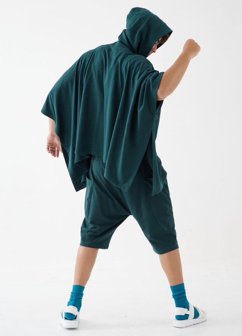 May include: A person wearing a dark green hooded poncho with matching shorts. The poncho has a long, flowing design and the shorts are loose-fitting.