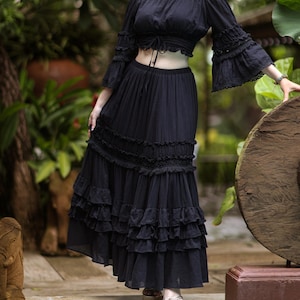 May include: A black off-the-shoulder crop top with long, ruffled sleeves and a matching black maxi skirt with multiple layers of ruffles.