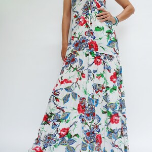 May include: White maxi dress with a floral pattern featuring red roses, blue paisley, and green leaves. The dress has spaghetti straps and a tiered skirt. The top has a tie detail at the bust.