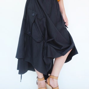 May include: A black asymmetrical skirt with a large cargo pocket and a tie detail. The skirt is made of a soft, flowing fabric and has a relaxed fit.