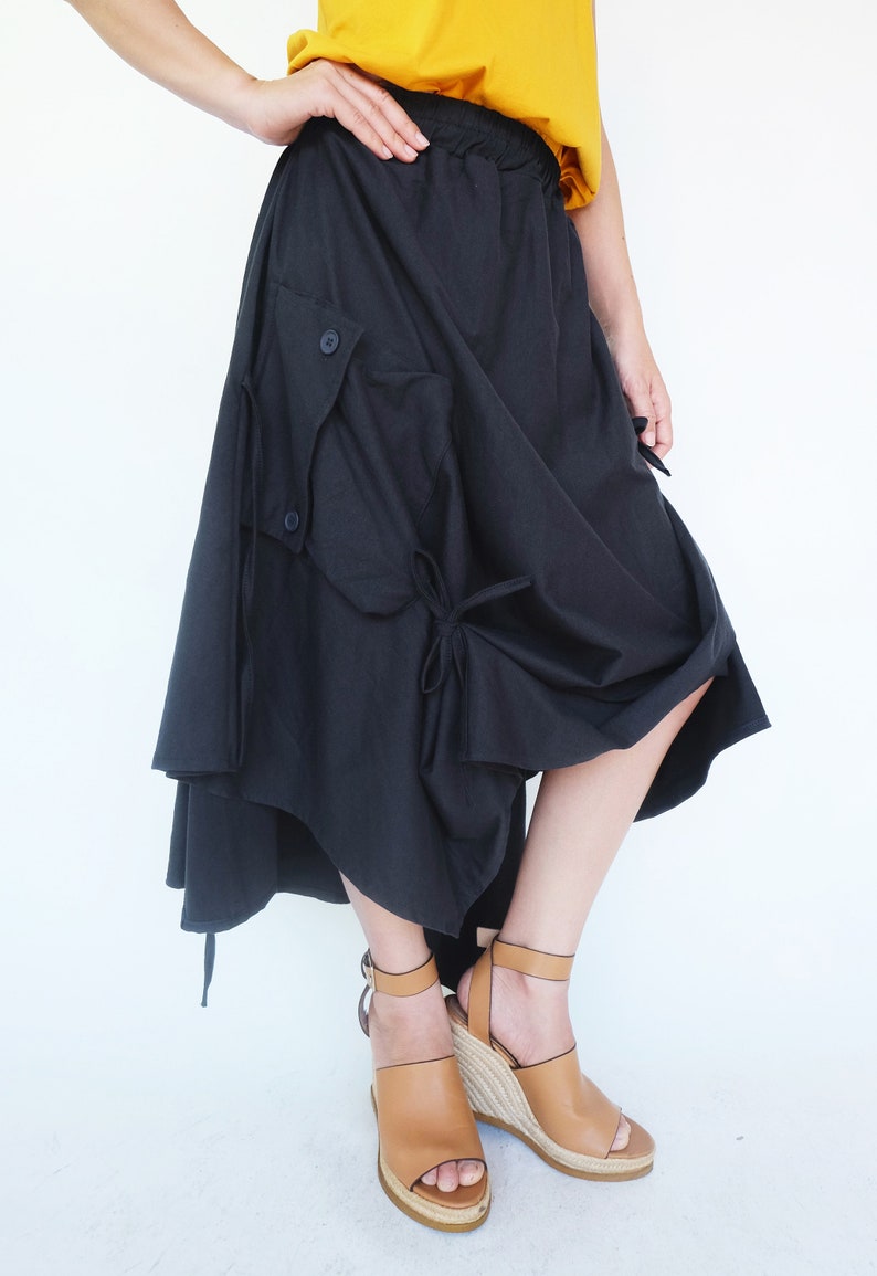 May include: A black asymmetrical skirt with a large cargo pocket and a tie detail. The skirt is made of a soft, flowing fabric and has a relaxed fit.