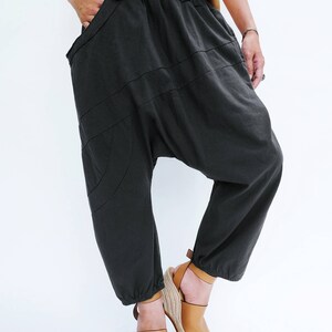 Pu&ograve; includere: Un paio di pantaloni neri larghi con gamba larga e vita elastica a pieghe. I pantaloni hanno un design unico con pi&ugrave; cuciture e una forma curva. La persona indossa i pantaloni con sandali a zeppa marroni.