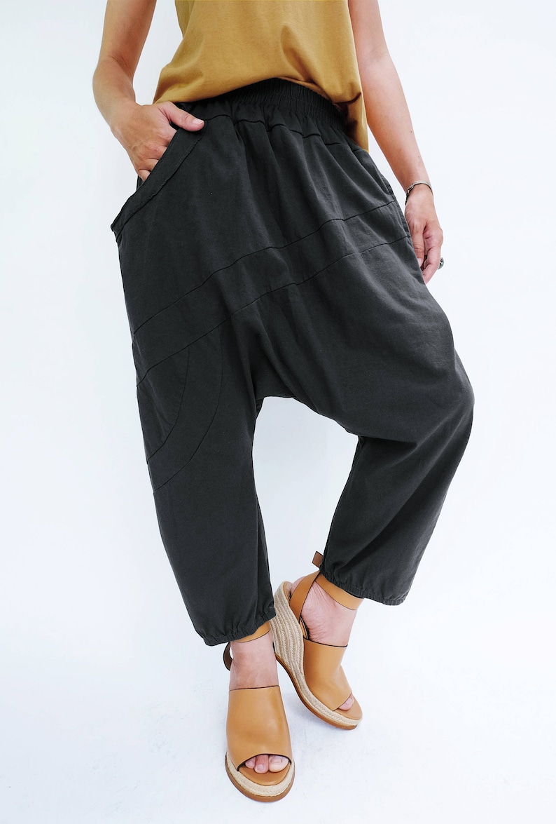 Pu&ograve; includere: Un paio di pantaloni neri larghi con gamba larga e vita elastica a pieghe. I pantaloni hanno un design unico con pi&ugrave; cuciture e una forma curva. La persona indossa i pantaloni con sandali a zeppa marroni.
