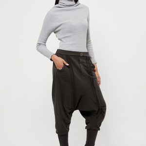 May include: A woman wearing a gray turtleneck sweater and brown, loose-fitting pants with a unique design. She is wearing black heeled boots.