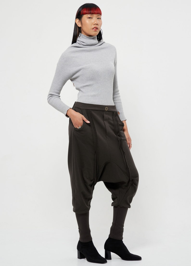 May include: A woman wearing a gray turtleneck sweater and brown, loose-fitting pants with a unique design. She is wearing black heeled boots.
