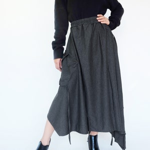 May include: A gray, asymmetrical skirt with a drawstring waist and a large cargo pocket on the left side. The skirt is paired with a black turtleneck sweater and black ankle boots.