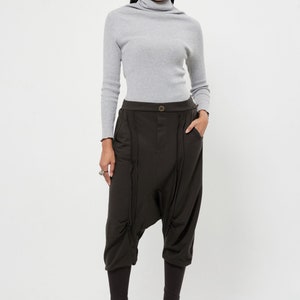 May include: A woman is wearing a gray turtleneck sweater and brown, loose-fitting pants with a unique design. The pants have a wide leg and a gathered detail at the knees.